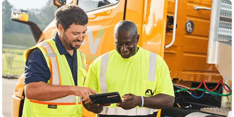 two FV Recycling staff members standing in front of a big truck looking at a tablet