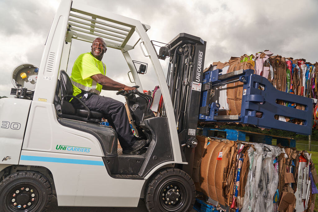 FV Recycling worker in a safety shirt driving a lift to pick up large bales of recycled material