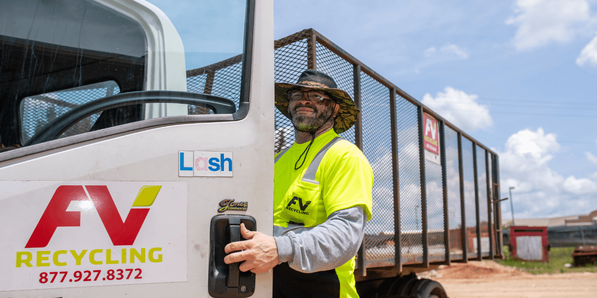 FV Recycling driver standing beside an open-top roll-off truck at a commercial recycling site