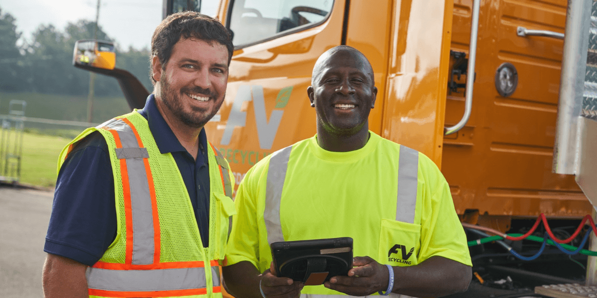 FV Recycling driver and team member in safety vests smiling beside an FV truck, one holding a tablet for pickup