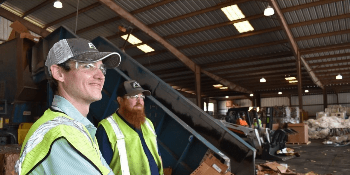 FV Recycling team members in safety vests at a cardboard baler conveyor in a commercial recycling facility
