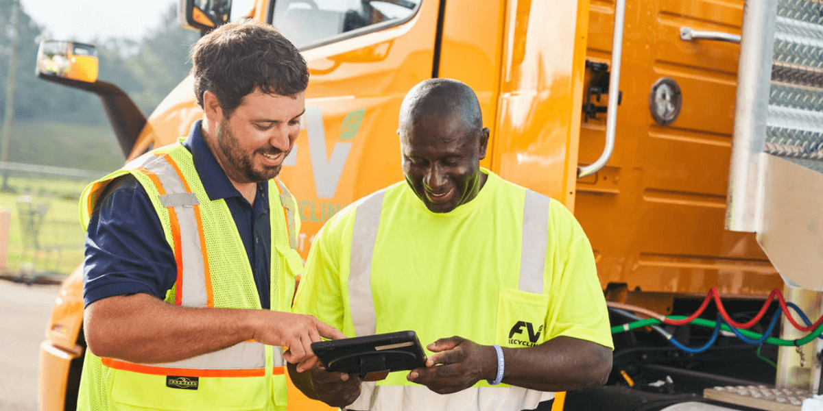 FV Recycling team member talking to customer, both looking at a tablet, with an FV truck in the background