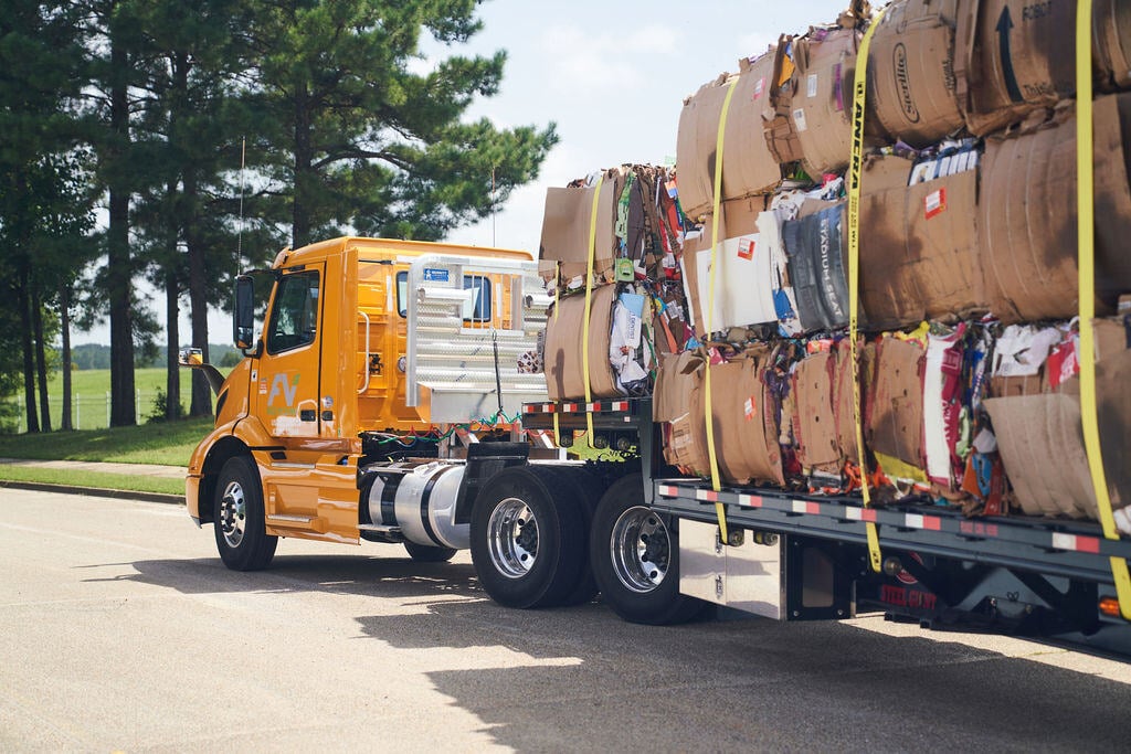 Yellow FV Recycling truck hauling large bales of recycled material