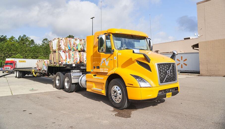 Yellow FV Recycling truck hauling large bales of recycled material behind the dock of a WalMart