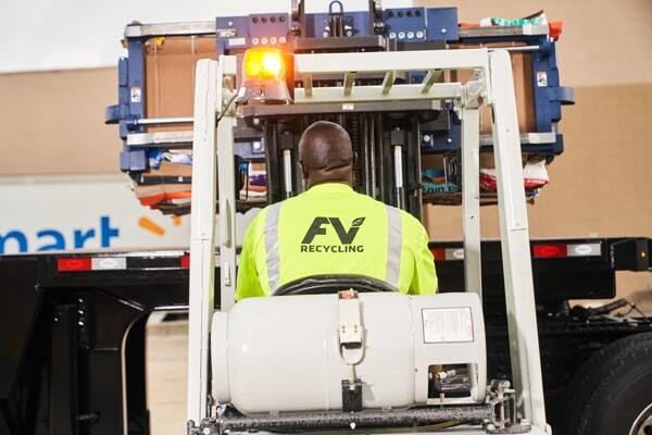 FV Recycling worker in a safety shirt driving a fork lift, lifting up a large blue recycling dumpster