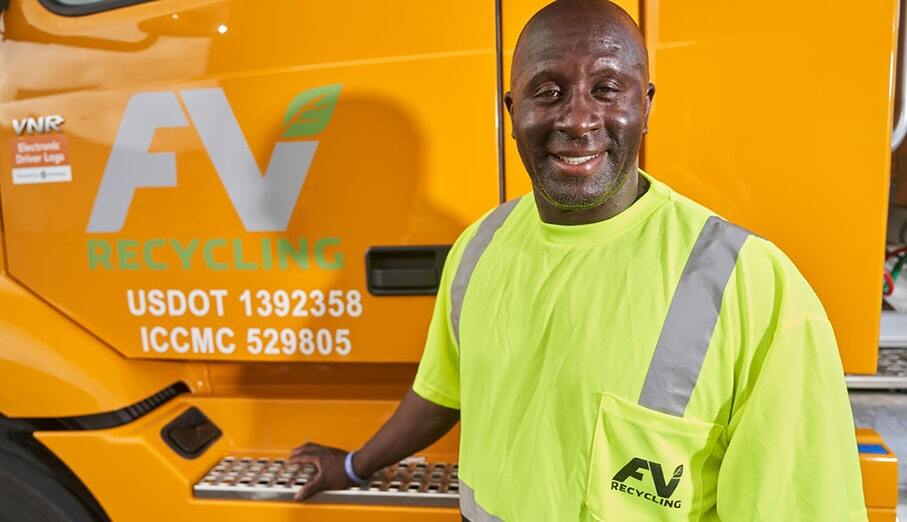 Male FV Recycling employee with FV yellow safety shirt on standing in front of the yellow FV Recycling 18-wheeler truck door