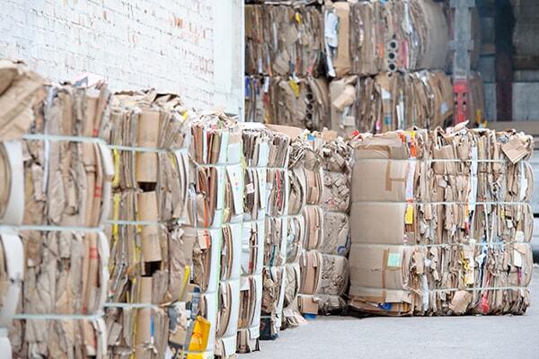 Stacks of baled recycle material spread out against a wall outside of a business taking up space