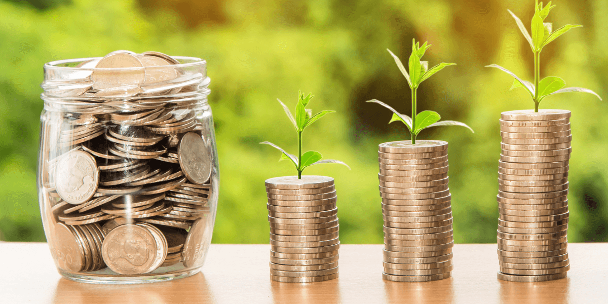 A jar of coins next to stacks of coins with plants growing out of the top of the stacks. 