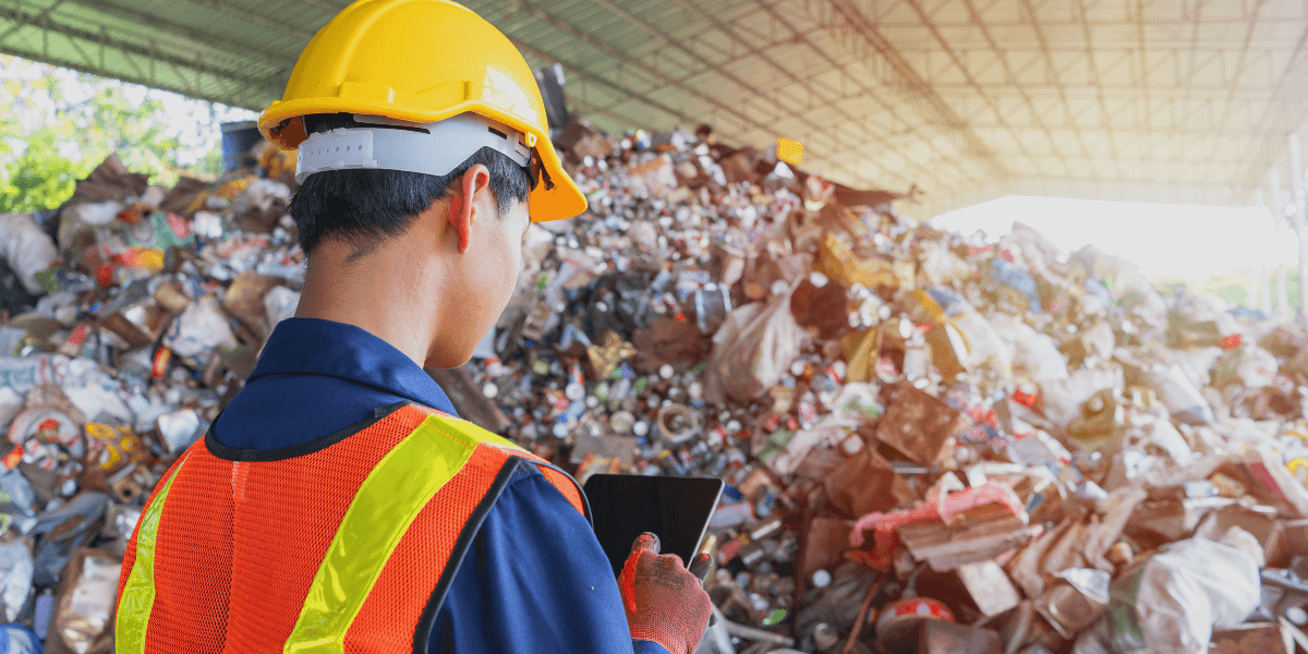 Recycling employee standing in front of recyclable materials on his ipad.