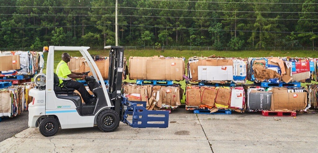 FV Recycling team member driving forklift carrying compacted cardboard on customer's site